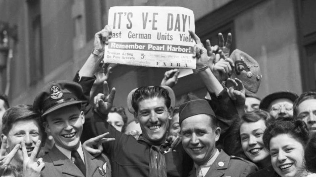 A group of people holding a newspaper with the headline 'VE DAY'.