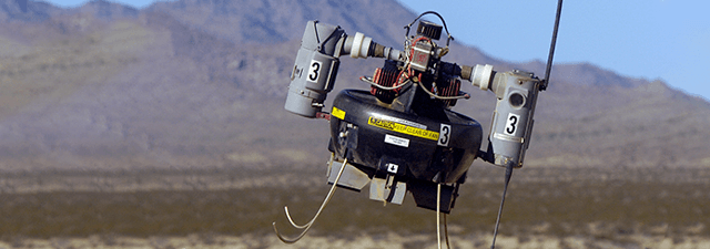 A small, black, unmanned aerial vehicle (UAV) with a yellow label and a white number 3 on its side, flying in a desert landscape.