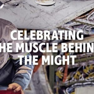 Two men in work attire, with the text "CELEBRATING THE MUSCLE BEHIND THE MIGHT" in the center.