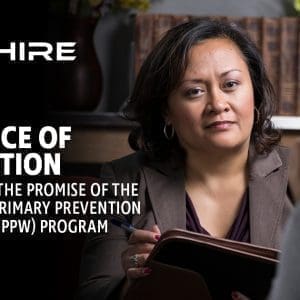 Aim Hire Episode 25: A woman in a brown blazer holding a tablet, with a person in the foreground and a bookshelf in the background.