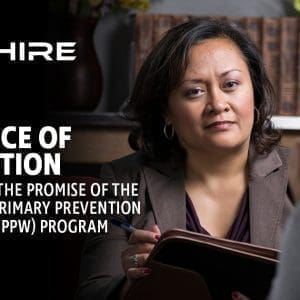 Aim Hire Episode 25: A woman in a brown blazer holding a tablet, with a person in the foreground and a bookshelf in the background.